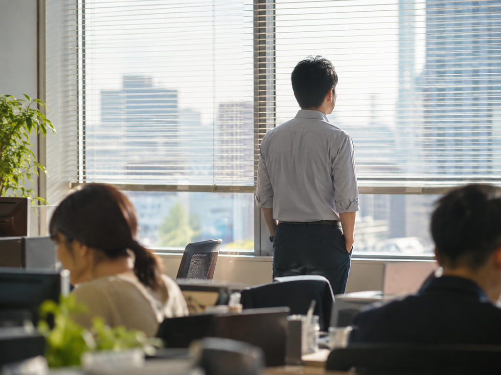 窓から外を見る会社員の背中