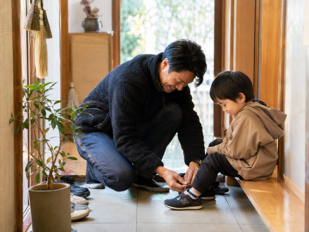土間で息子の靴紐を結ぶ父親